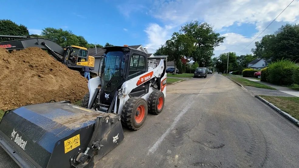 Bobcat skid-steer loader carrying a bucket of soil on a residential street in Rochester NY