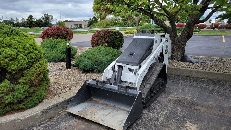 Compact track loader with a bucket on a paved residential driveway in Rochester NY