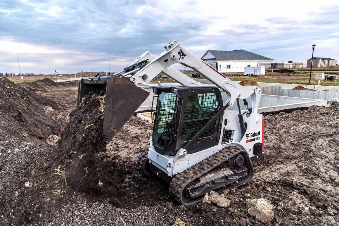 Bobcat compact track loader moving material beside a dirt pile on a Rochester NY job site