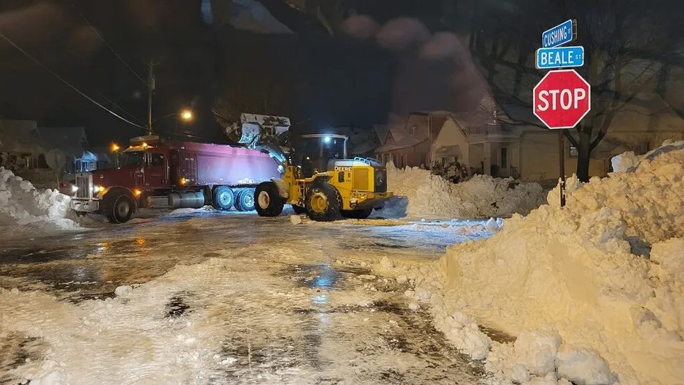 Yellow wheel loader clearing large snow piles overnight on a Rochester NY street